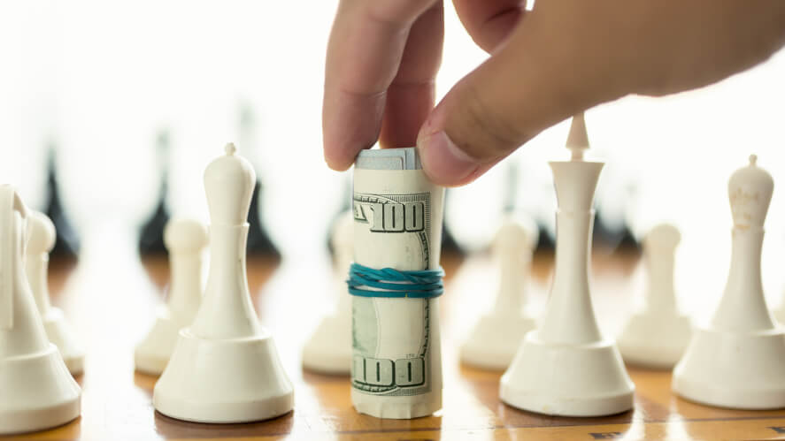 A hand playing a money pile in a chess table represents for finding the best step to find investors