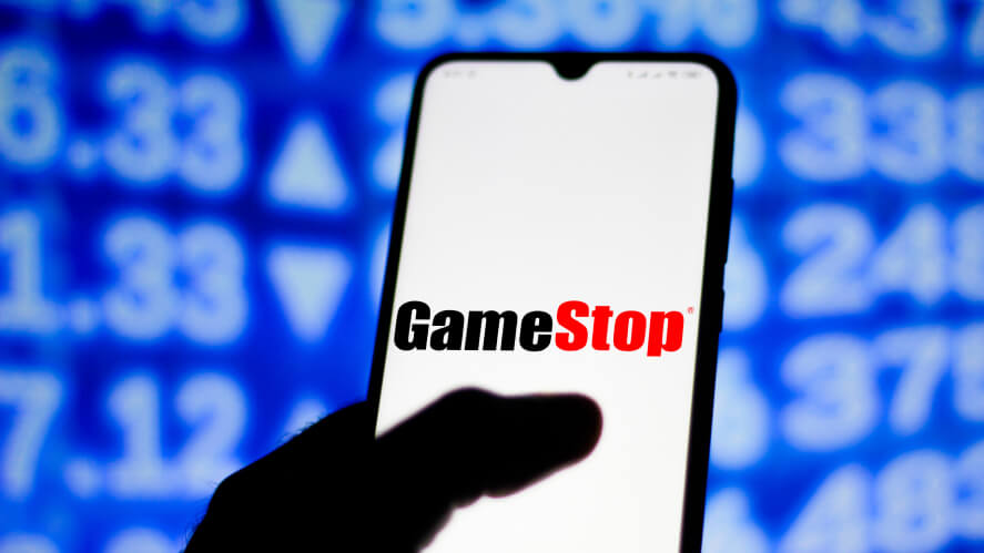 A person holding a phone with GameStop on the screen with stock background.