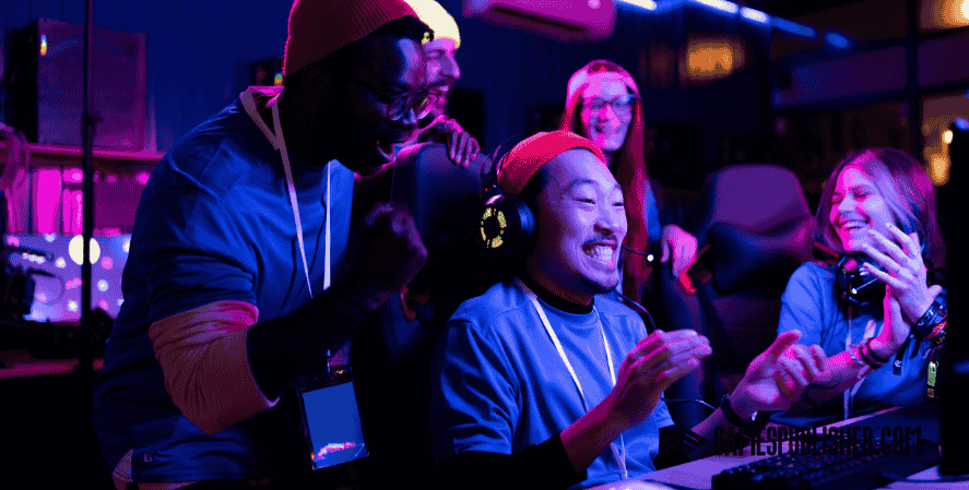 Indie game development team celebrating together after a successful playtest or game launch in a neon-lit gaming room.